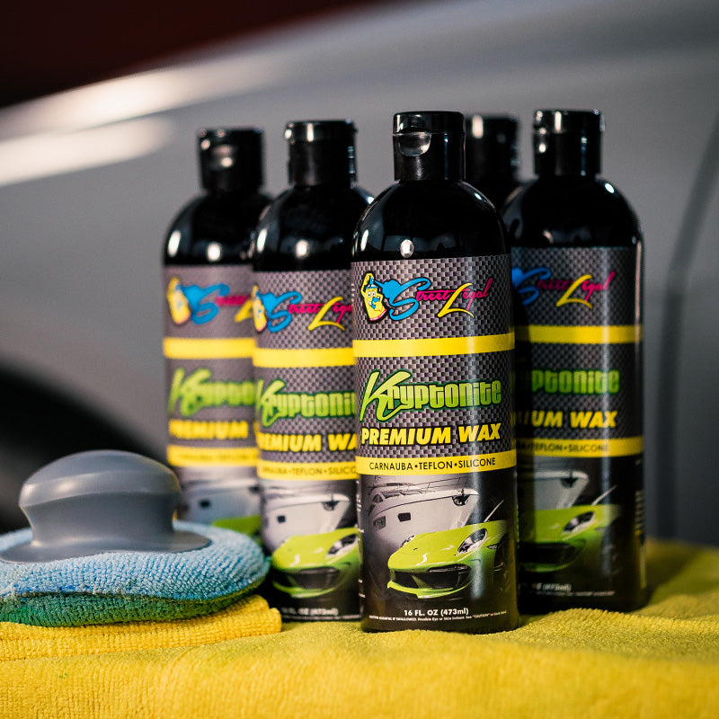 6 bottles of Street Legal Kryptonite Premium Wax on table with polishing pad and cloth