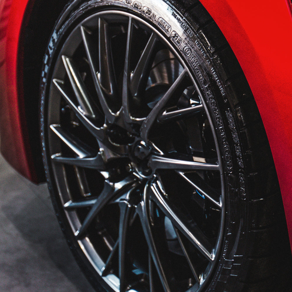 Shiny black tire on a red car treated with The Ultimate Wet Tire Shine from The Shield Xtreme Protector Bundle, 1 Gallon Each.